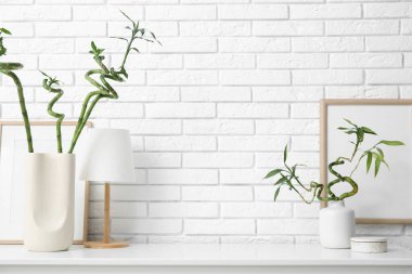 Bambu saplı vazolar ve beyaz tuğla duvarın yanındaki çekmecelerin üzerinde lamba, yakın plan.