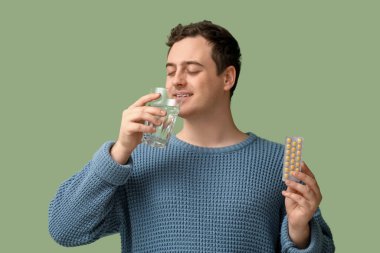 Yeşil arka planda haplar ve bir bardak suyla mutlu genç bir adam.
