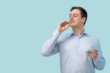 Mavi arka planda haplı ve bir bardak suyu olan mutlu genç bir adam.