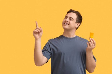 Sarı arka planda bir şeyi işaret eden haplarla dolu bir kutu taşıyan mutlu genç adam.