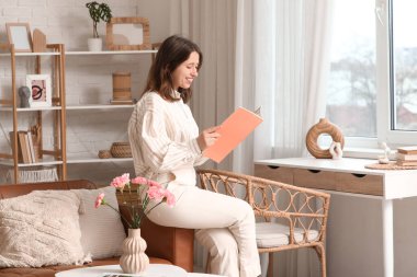 Oturma odasındaki kanepede dergi okuyan mutlu genç kadın.