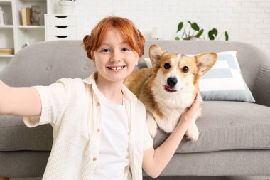 Kanepede Corgi köpeği olan kızıl saçlı genç bir kız evde selfie çekiyor.