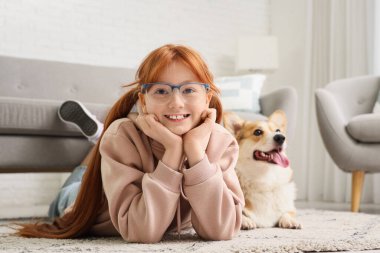Güzel Corgi köpeği olan kızıl saçlı genç bir kız evde halıya uzanmış yatıyor.