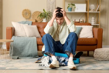 Stresli erkek turist valizini evde kapatmaya çalışıyor.