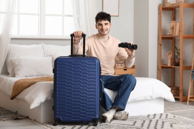 Dürbünlü ve bavullu bir erkek turist yatak odasında.