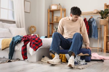 Erkek turist yatak odasında valizini kapatmaya çalışıyor.