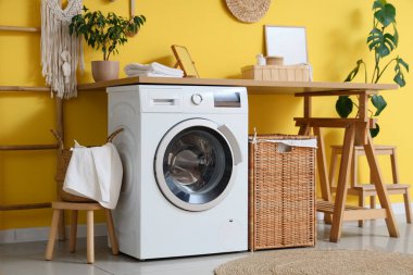 Modern çamaşır makinesi, hasır sepeti ve banyo aksesuarları olan şık bir çamaşırhane.