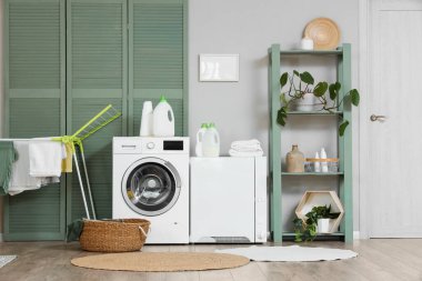 Modern çamaşır makinesi, kurutma makinesi ve banyo aksesuarları olan şık bir çamaşırhane.