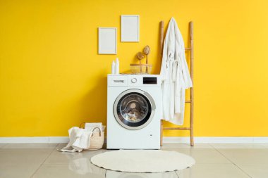 Modern çamaşır makinesi, hasır sepeti ve banyo aksesuarları olan şık bir çamaşırhane.