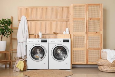 Modern çamaşır makineleri, hasır sepeti ve banyo aksesuarları olan şık bir çamaşırhane.