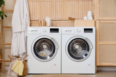 Modern çamaşır makineleri, hasır sepeti ve banyo aksesuarları olan şık bir çamaşırhane.