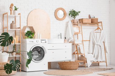 Modern çamaşır makinesi, hasır sepeti, raf ünitesi ve banyo aksesuarları olan şık bir çamaşırhane.