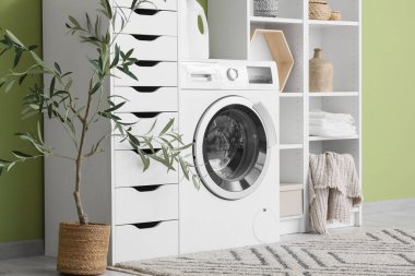 Modern çamaşır makinesi, raf ünitesi ve banyo aksesuarları olan şık bir çamaşırhane.