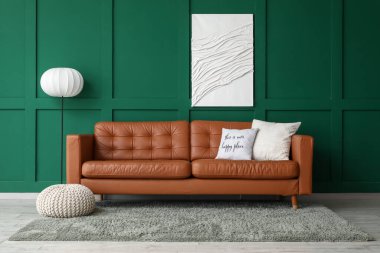 Yumuşak yastıklı kahverengi deri kanepe ve oturma odasındaki yeşil duvarın yanında yer lambası