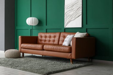 Yumuşak yastıklı kahverengi deri kanepe ve oturma odasındaki yeşil duvarın yanında yer lambası