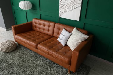 Yumuşak yastıklı kahverengi deri kanepe ve oturma odasındaki yeşil duvarın yanında yer lambası