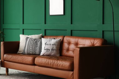 Oturma odasındaki yeşil duvarın yanında yumuşak yastıklı kahverengi deri kanepe.