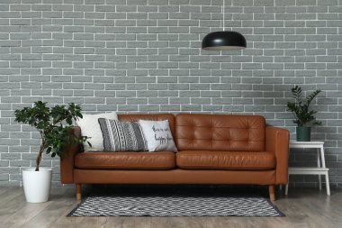 Yumuşak yastıklı kahverengi deri kanepe ve oturma odasındaki gri tuğla duvarın yanında bitkiler.