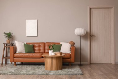 Kahverengi deri kanepe, ahşap masa ve oturma odasındaki gri duvarın yanında yer lambası.