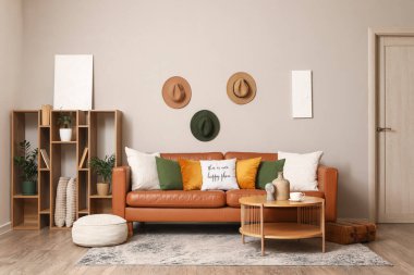 Oturma odasındaki gri duvarın yanında yumuşak puf ve raf üniteli kahverengi deri kanepe.