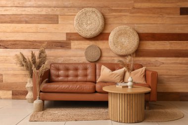 Yumuşak yastıklı kahverengi deri kanepe ve oturma odasındaki tahta duvarın yanındaki masa.