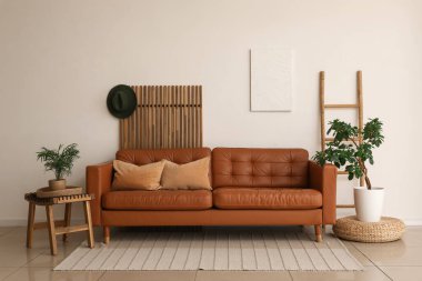 Yumuşak yastıklı kahverengi deri kanepe ve oturma odasındaki beyaz duvarın yanında bitkiler.