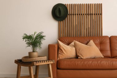 Yumuşak yastıklı kahverengi deri kanepe ve oturma odasındaki beyaz duvarın yanında çiçek.