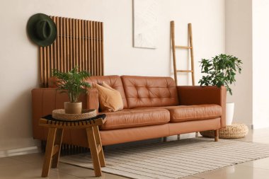 Yumuşak yastıklı kahverengi deri kanepe ve oturma odasındaki beyaz duvarın yanında bitkiler.