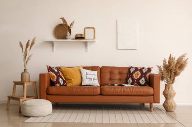 Yumuşak yastıklı kahverengi deri kanepe ve oturma odasındaki beyaz duvarın yanında puf.