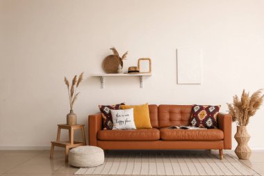 Yumuşak yastıklı kahverengi deri kanepe ve oturma odasındaki beyaz duvarın yanında puf.