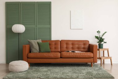 Kahverengi deri kanepe, yumuşak puf ve beyaz duvarın yanındaki oturma odası.