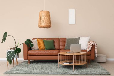 Kahverengi deri kanepe ve oturma odasındaki bej duvarın yanında modern dizüstü bilgisayarı olan ahşap masa.