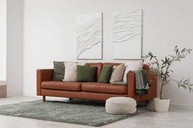 Yumuşak yastıklı kahverengi deri kanepe ve oturma odasındaki beyaz duvarın yanında puf.