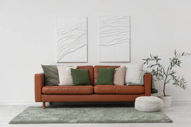 Yumuşak yastıklı kahverengi deri kanepe ve oturma odasındaki beyaz duvarın yanında puf.