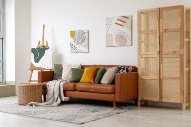 Yumuşak yastıklı kahverengi deri kanepe ve oturma odasındaki beyaz duvarın yanındaki hasır masa.