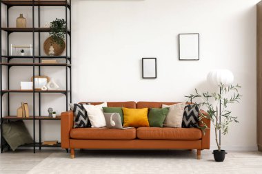 Yumuşak yastıklı kahverengi deri kanepe ve oturma odasındaki beyaz duvarın yanında modern laptop.