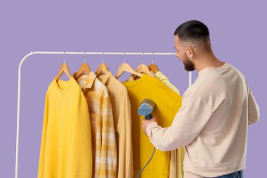 Leylak arka planda buharlı giysiler giyen genç bir adam.