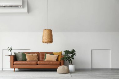 Kahverengi deri kanepe ve beyaz duvarın yanındaki bitkiler.