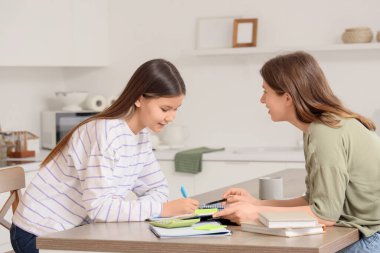 Genç kız mutfaktaki masada öğretmeniyle Matematik okuyor.