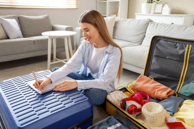 Bavulu olan kadın turist evde toplanacak eşyaların listesini yazıyor.