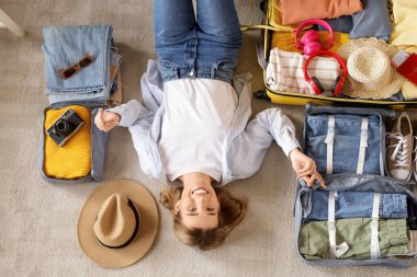 Bavullu ve katlanmış elbiseli bir kadın turist halının üzerinde yatıyor.