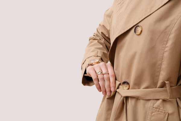Женщина в плаще с золотыми наручными часами на белом фоне, крупным планом