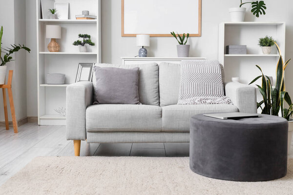 Interior of living room with grey sofa, pouf and shelf units