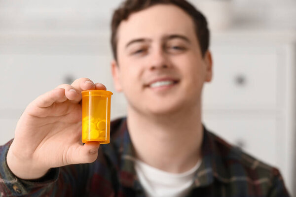 Счастливый молодой человек с бутылкой таблеток дома, крупным планом