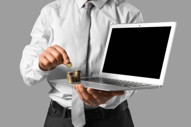 Dizüstü bilgisayarı ve gri arka planda parası olan iş adamı, yakın plan.