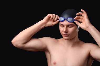 Erkek yüzücü koyu arkaplana karşı gözlük takıyor