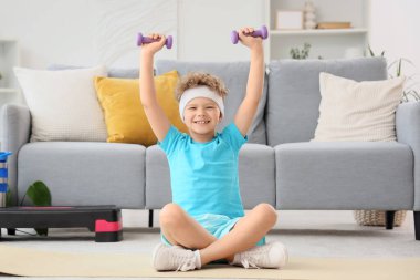 Sportif küçük çocuk evde dambıllarla egzersiz yapıyor.