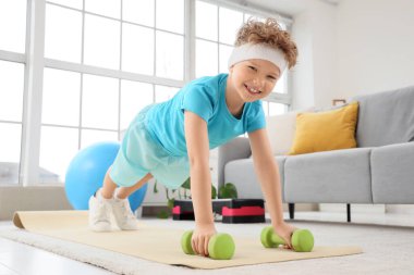 Sportif küçük çocuk evde dambıllarla egzersiz yapıyor.