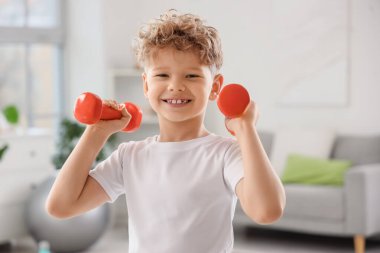 Sportif küçük çocuk evde dambıllarla egzersiz yapıyor.