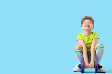 Sportif küçük çocuk mavi arka planda ağır dambılları kaldırmaya çalışıyor.